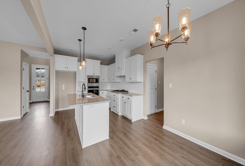 Kitchen featuring stainless steel appliances, visible vents, white cabinetry, hanging light fixtures, and a center island with sink