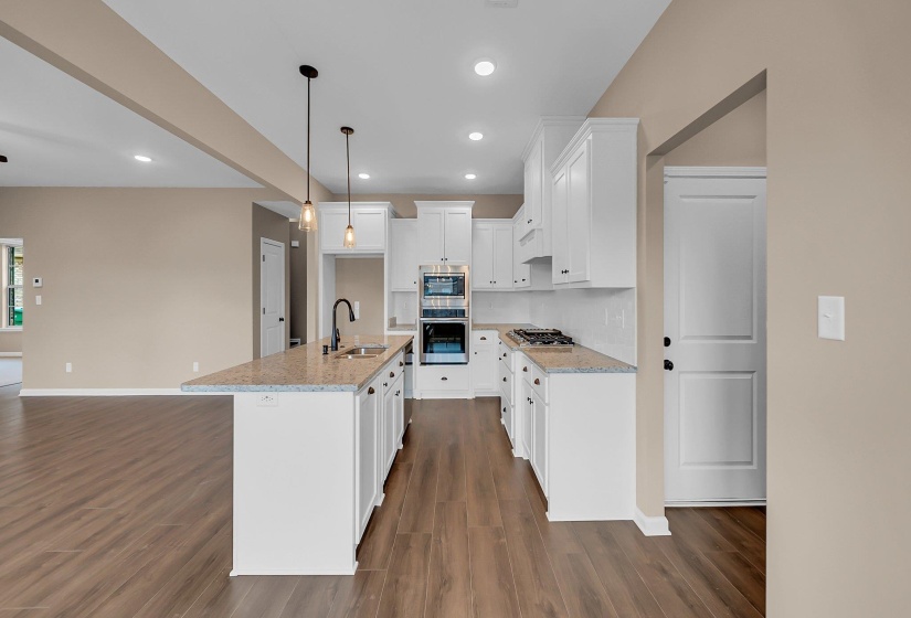 Kitchen featuring pendant lighting, stainless steel appliances, white cabinets, a sink, and an island with sink