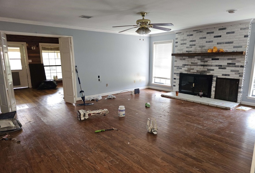 Unfurnished living room featuring crown molding, a ceiling fan, hardwood / wood-style floors, and a brick fireplace