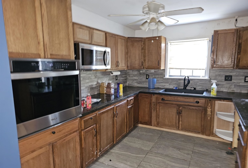Kitchen featuring appliances with stainless steel finishes, backsplash, ceiling fan, and dark countertops