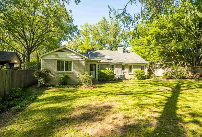 Back of house with fence, a lawn, a chimney, and brick siding
