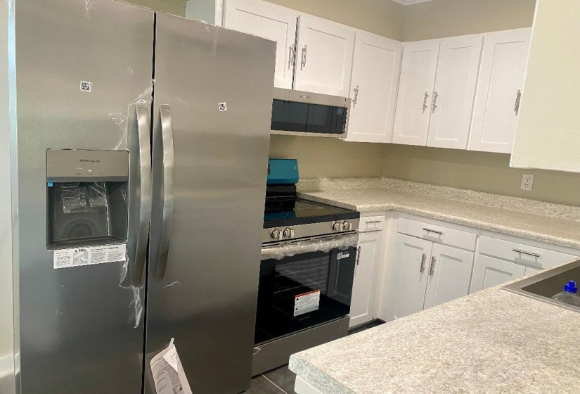 Kitchen with appliances with stainless steel finishes, white cabinetry, and light countertops