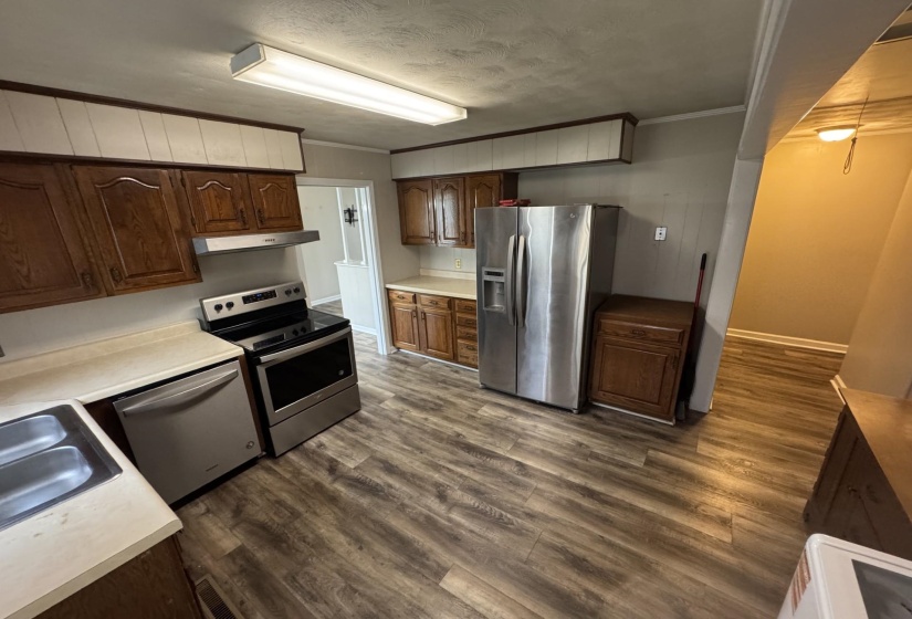 Kitchen featuring appliances with stainless steel finishes, under cabinet range hood, crown molding, dark wood-style floors, and light countertops