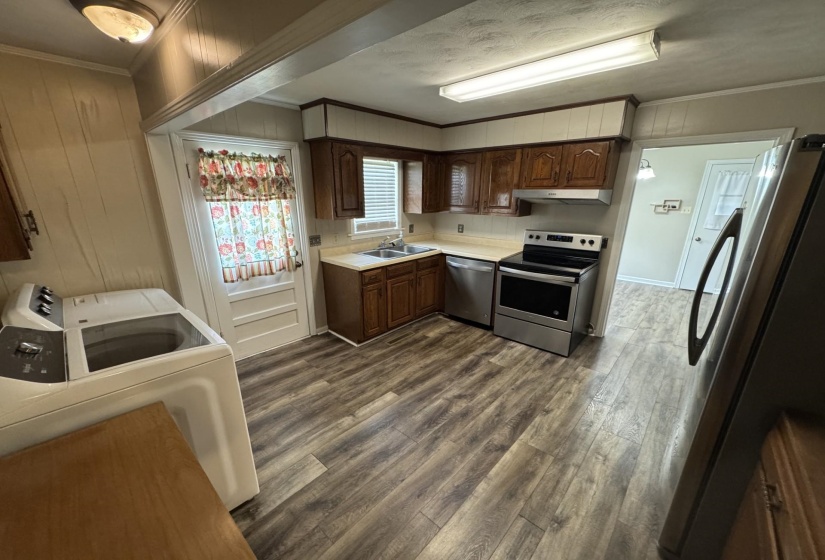 Kitchen featuring stainless steel appliances, ornamental molding, exhaust hood, dark wood-style flooring, and light countertops
