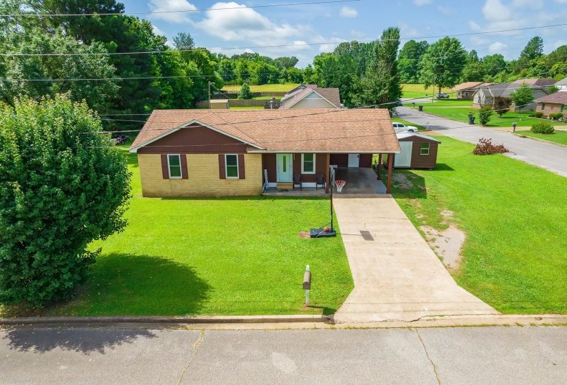 Ranch-style home with concrete driveway, an attached carport, a shingled roof, a front yard, and a porch