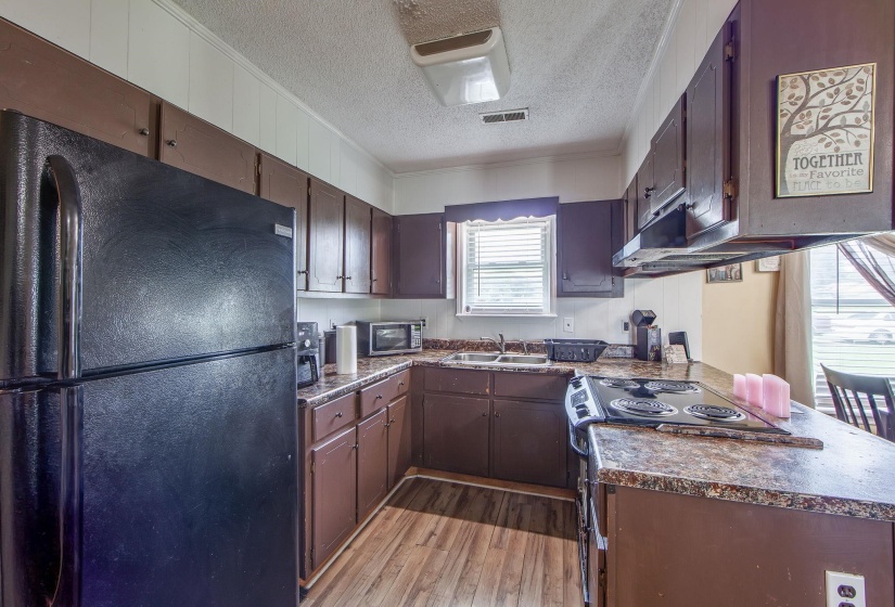 Kitchen with freestanding refrigerator, a textured ceiling, light wood-style flooring, stainless steel microwave, and electric stove