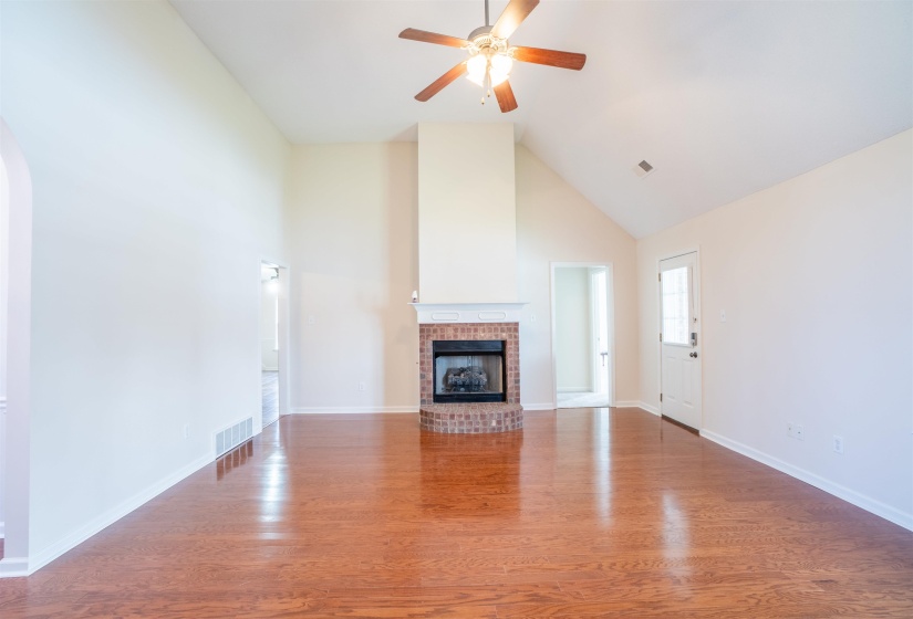 Unfurnished living room featuring high vaulted ceiling, ceiling fan, a brick fireplace, wood finished floors, and arched walkways