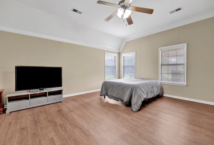 Bedroom featuring crown molding, wood finished floors, lofted ceiling, and a ceiling fan