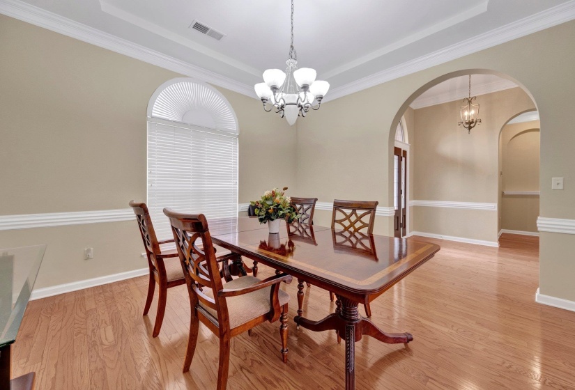 Dining area with a chandelier, arched walkways, a tray ceiling, light wood finished floors, and crown molding