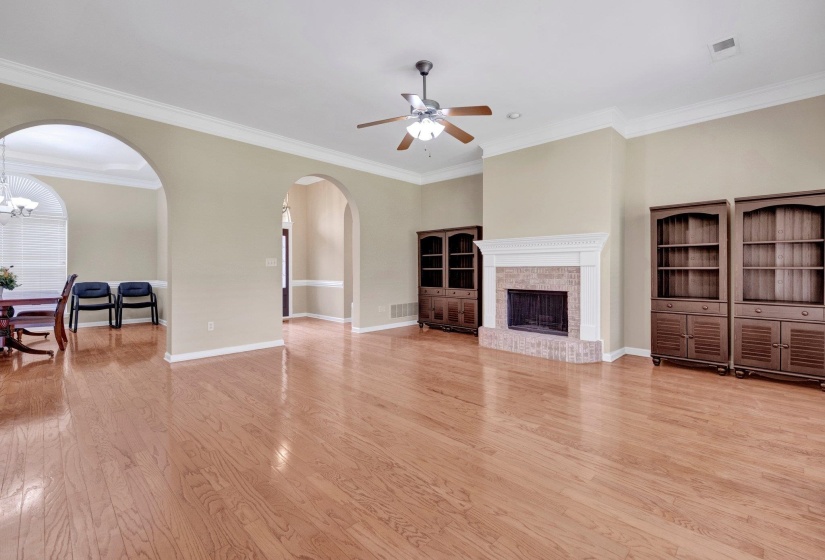 Unfurnished living room featuring arched walkways, ceiling fan, a fireplace, crown molding, and light wood-style flooring