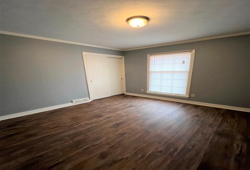 Unfurnished bedroom featuring dark wood-style floors, crown molding, and a closet