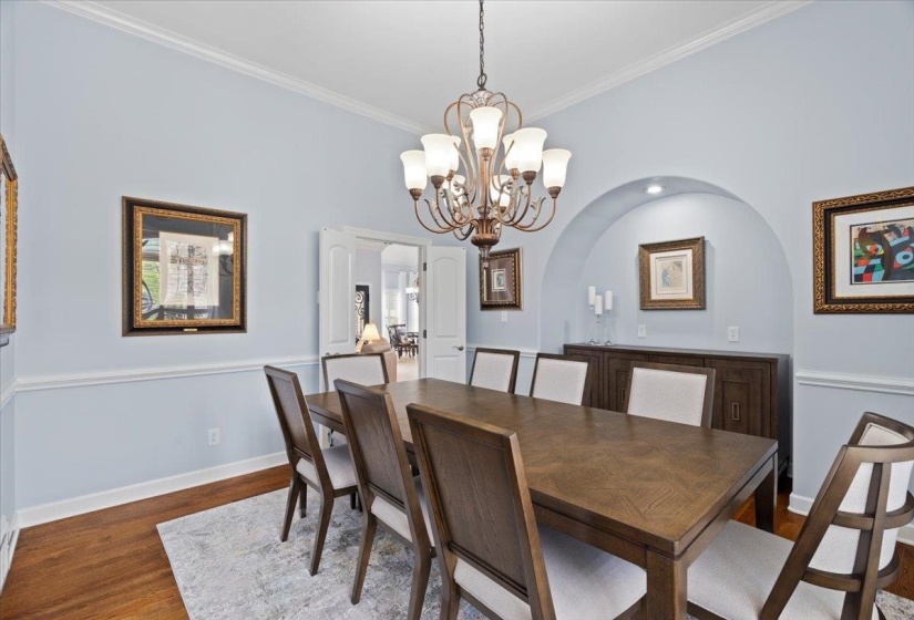 Dining area with a chandelier, wood finished floors, arched walkways, and crown molding