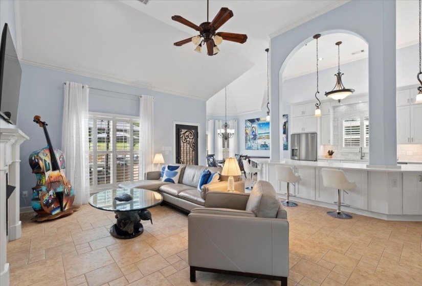 Living area featuring a chandelier, stone tile floors, a ceiling fan, crown molding, and high vaulted ceiling