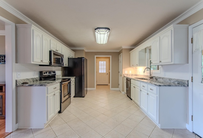 Kitchen with appliances with stainless steel finishes, ornamental molding, white cabinetry, light stone countertops, and light tile patterned floors