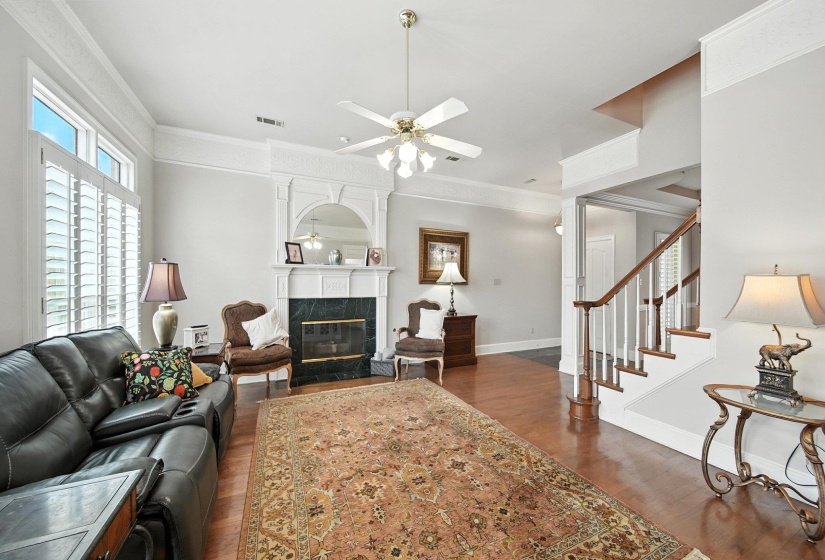Living area featuring dark wood finished floors, a ceiling fan, a high end fireplace, ornamental molding, and stairway