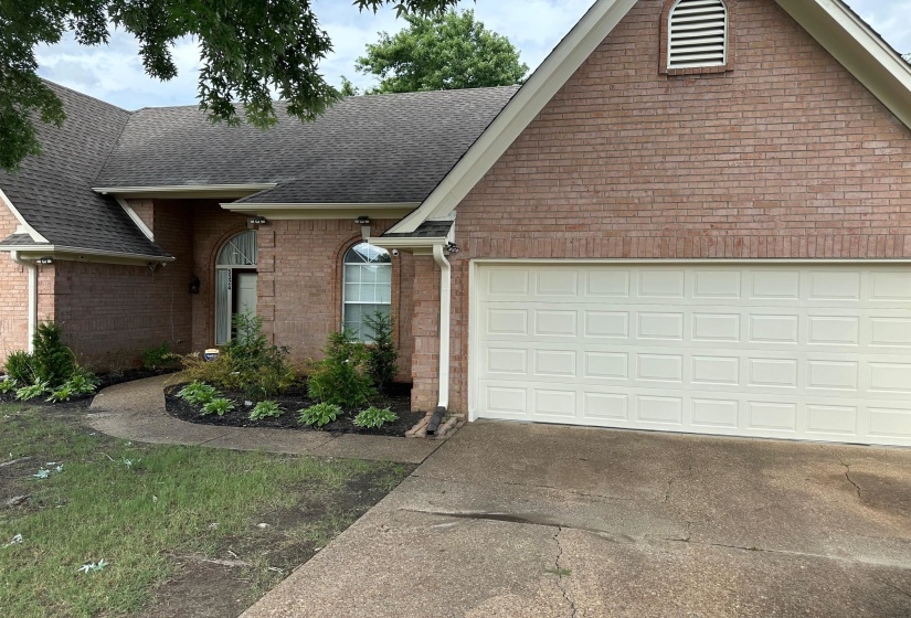 View of front facade with roof with shingles, a garage, concrete driveway, and brick siding