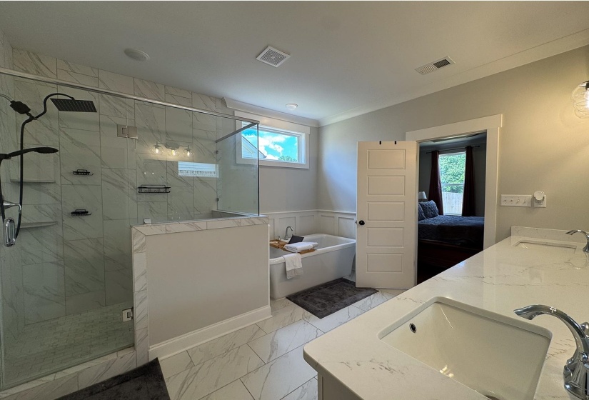 Full bath featuring a garden tub, marble look tiles, double vanity, a marble finish shower, and plenty of natural light