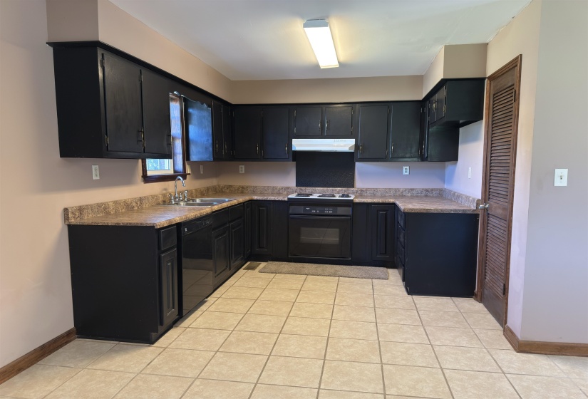 Kitchen with dark cabinets, light tile patterned floors, dishwasher, and under cabinet range hood
