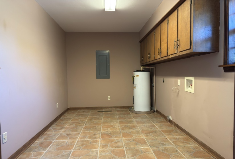 Washroom featuring electric panel, electric water heater, washer hookup, light tile patterned floors, and cabinet space