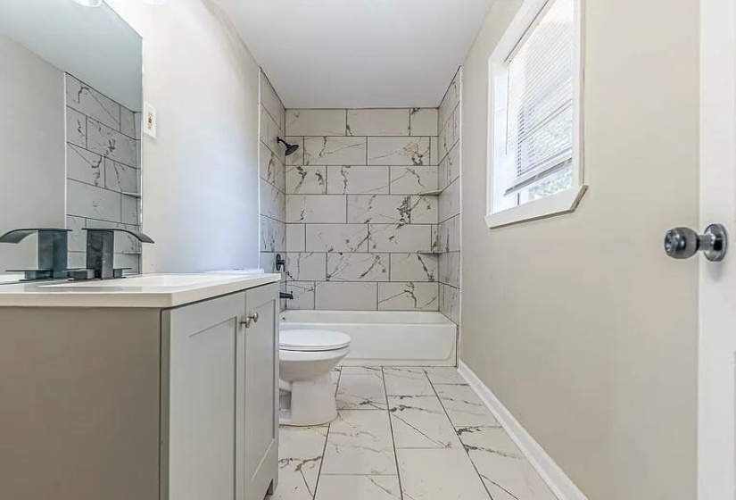Bathroom with marble look tile flooring, vanity, and shower / tub combination