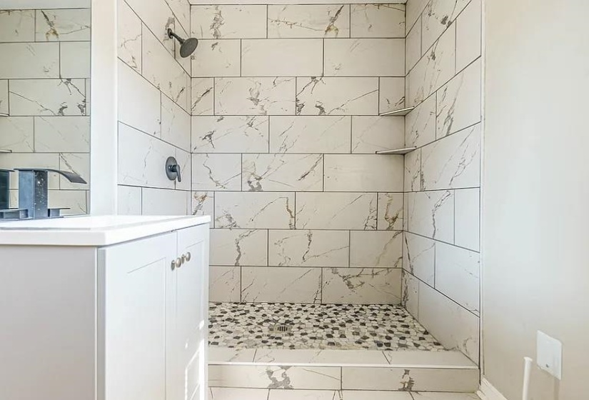 Full bath featuring a tile shower, vanity, and marble finish floors