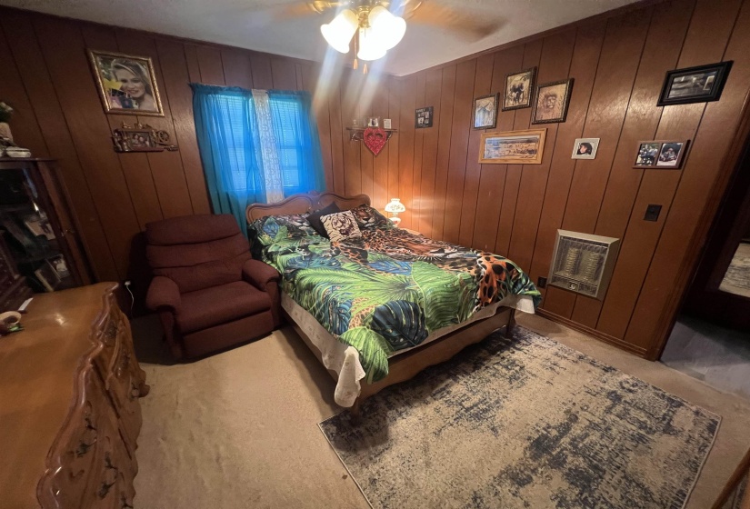 Bedroom featuring ceiling fan, wooden walls, and light colored carpet