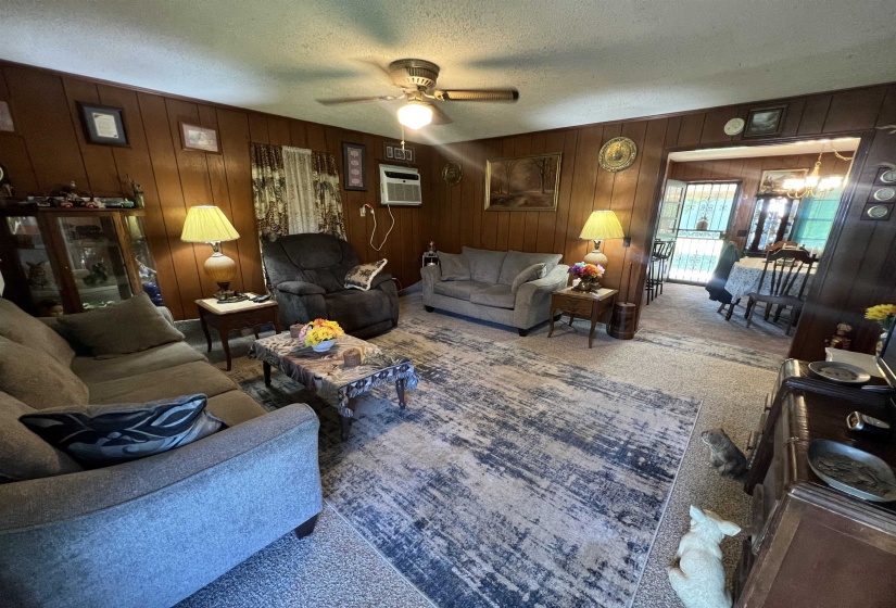 Carpeted living room featuring wood walls, an AC wall unit, a textured ceiling, and ceiling fan
