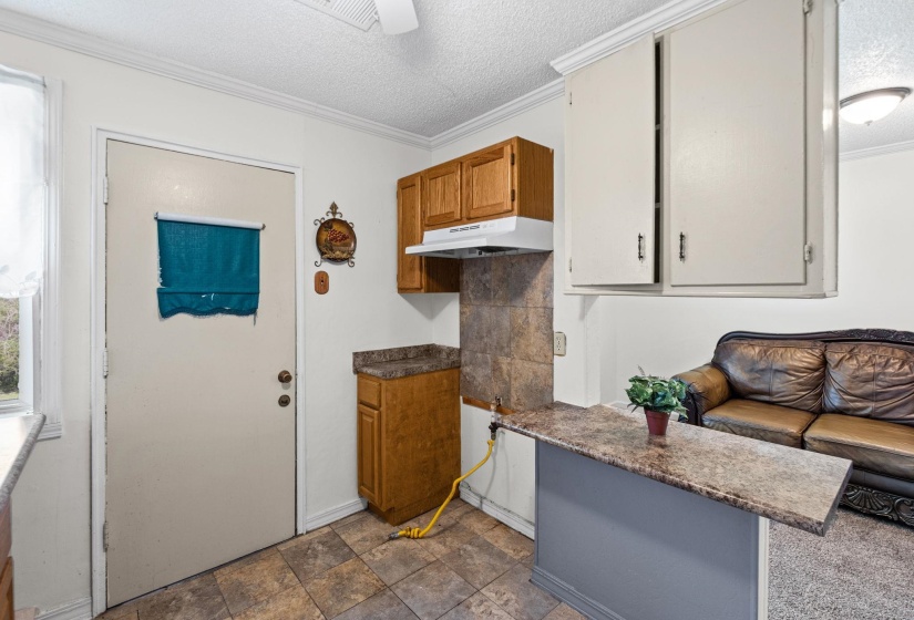 Kitchen featuring a textured ceiling, stone finish flooring, dark countertops, ornamental molding, and a ceiling fan