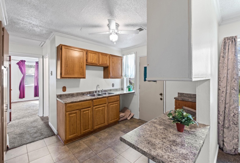 Kitchen with wood finish cabinetry, a textured ceiling, ornamental molding, dark colored carpet, and a ceiling fan