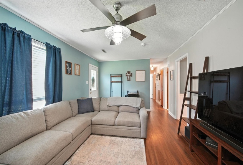 Living area featuring wood finished floors, plenty of natural light, ceiling fan, a textured ceiling, and crown molding