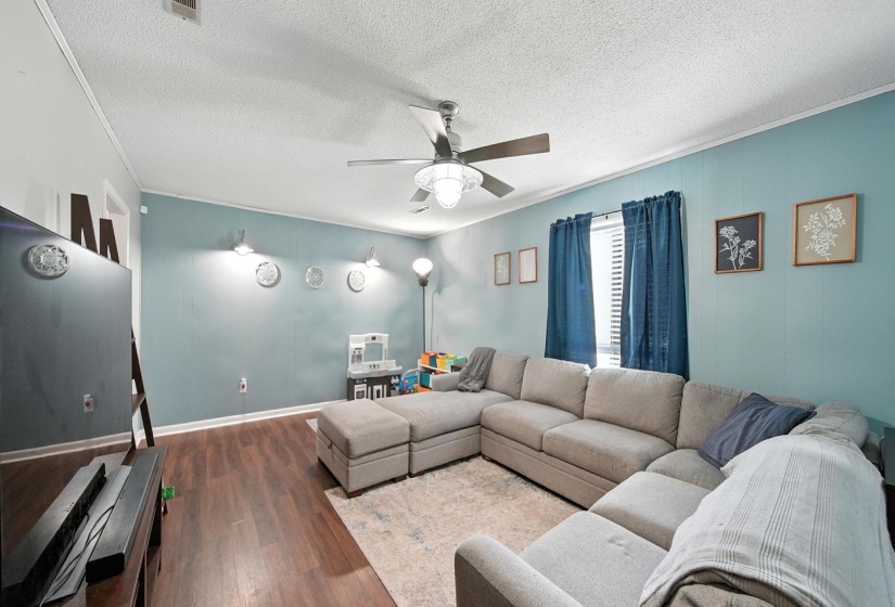 Living room featuring crown molding, dark wood-type flooring, a ceiling fan, and a textured ceiling