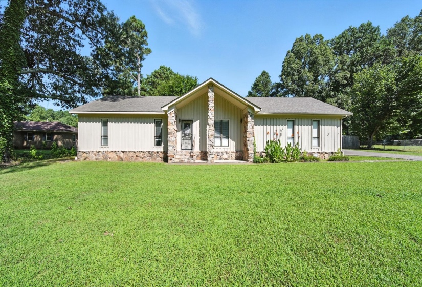 View of front of house with a front yard, a shingled roof, and stone siding