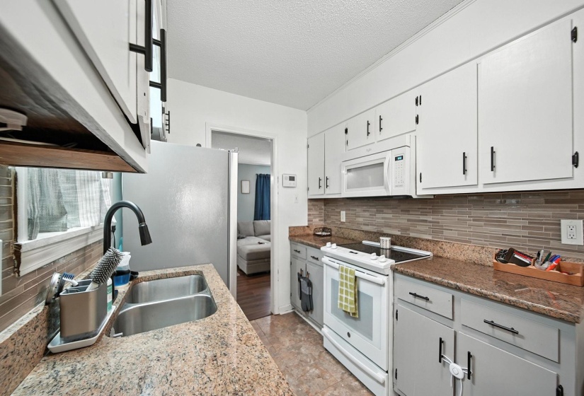 Kitchen featuring white appliances, decorative backsplash, white cabinets, and a textured ceiling