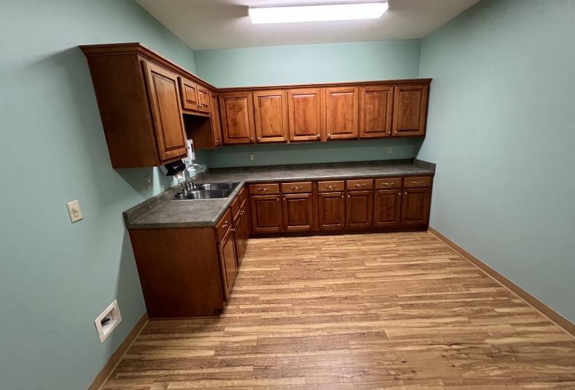 Kitchen with baseboards, dark countertops, light wood-style flooring, and a sink