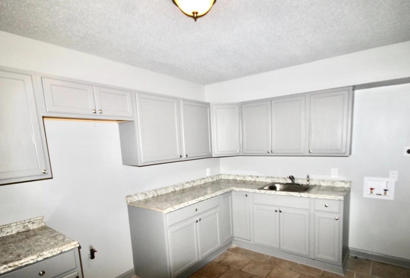 Laundry room featuring hookup for a washing machine, a textured ceiling, cabinet space, dark stone finish floors, and baseboards