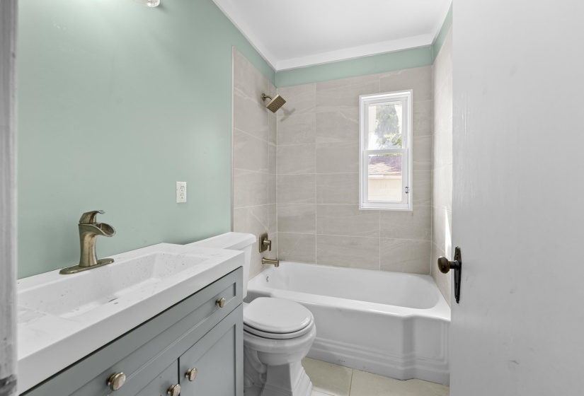 The upgraded bathroom showcases ceramic tile flooring, a modern vanity, and a tub/shower surround with tasteful tile.
