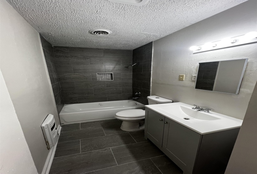 Full bath with a textured ceiling, toilet, tub / shower combination, vanity, and heating unit