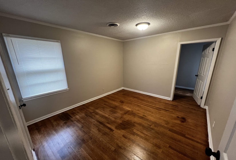 Empty room featuring wood finished floors, baseboards, a textured ceiling, and ornamental molding