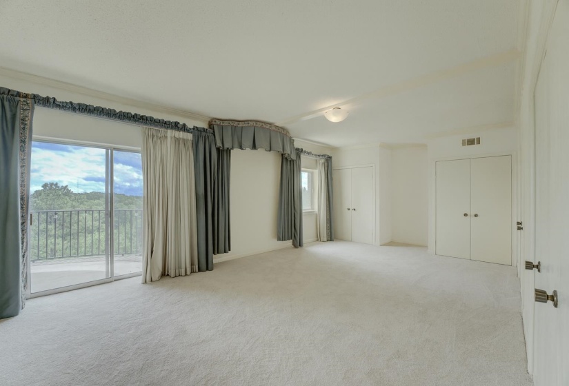 This airy bedroom features a neutral color scheme and plush carpet, 4 closets, and double glass doors that frame a beautiful balcony view and fill the space with natural light.