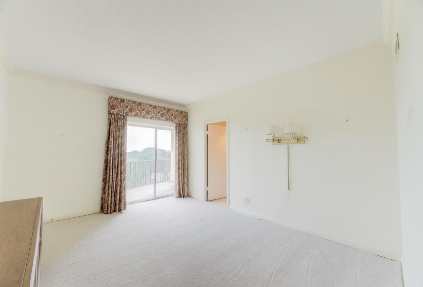 Soft carpet underfoot, walk-in closet, and a calming neutral color palette create a restful atmosphere in this spacious bedroom. Double glass doors open to the balcony, inviting in fresh air and natural light.