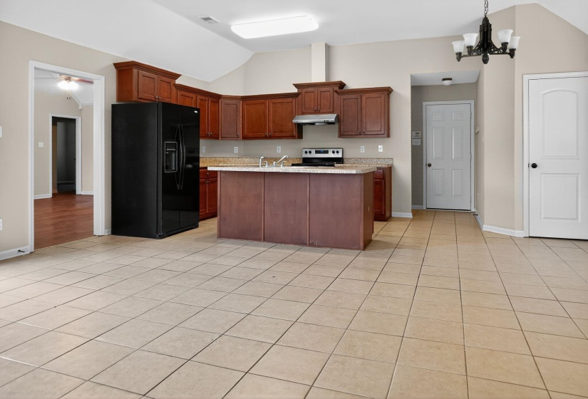 Kitchen with black fridge, pendant lighting, light tile patterned floors, lofted ceiling, and a chandelier