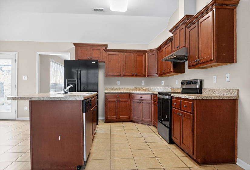 Kitchen with appliances with stainless steel finishes, light tile patterned floors, light countertops, under cabinet range hood, and an island with sink