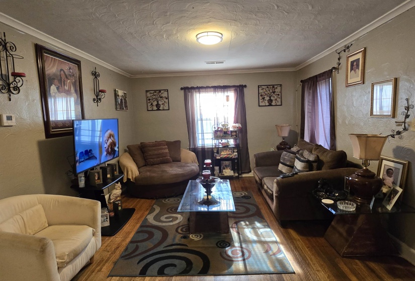 Living room with ornamental molding, a textured ceiling, a textured wall, and wood finished floors