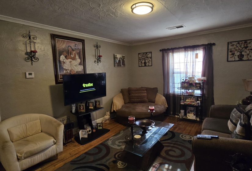 Living room featuring a textured wall, wood finished floors, ornamental molding, and a textured ceiling