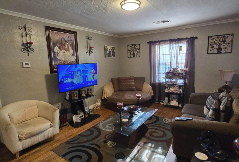 Living area with a textured wall, wood finished floors, ornamental molding, and a textured ceiling