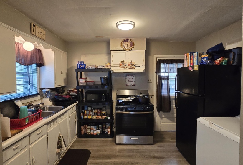 Kitchen with white cabinets, dark wood-style floors, black appliances, light countertops, and plenty of natural light