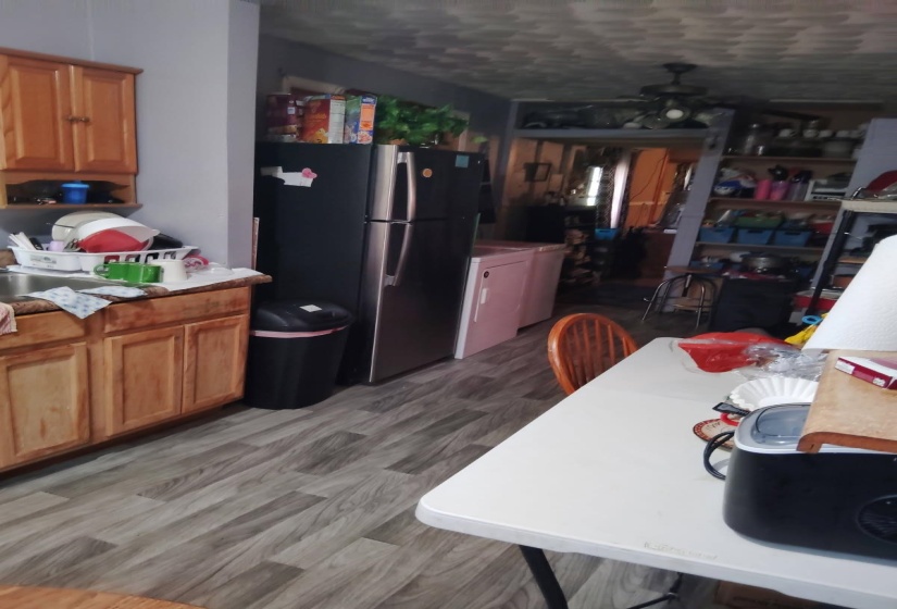 Kitchen featuring a ceiling fan, freestanding refrigerator, brown cabinetry, light countertops, and washer / clothes dryer