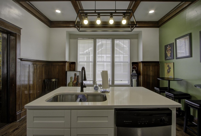 Kitchen featuring dark wood-style flooring, dishwasher, white cabinets, ornamental molding, and a center island with sink