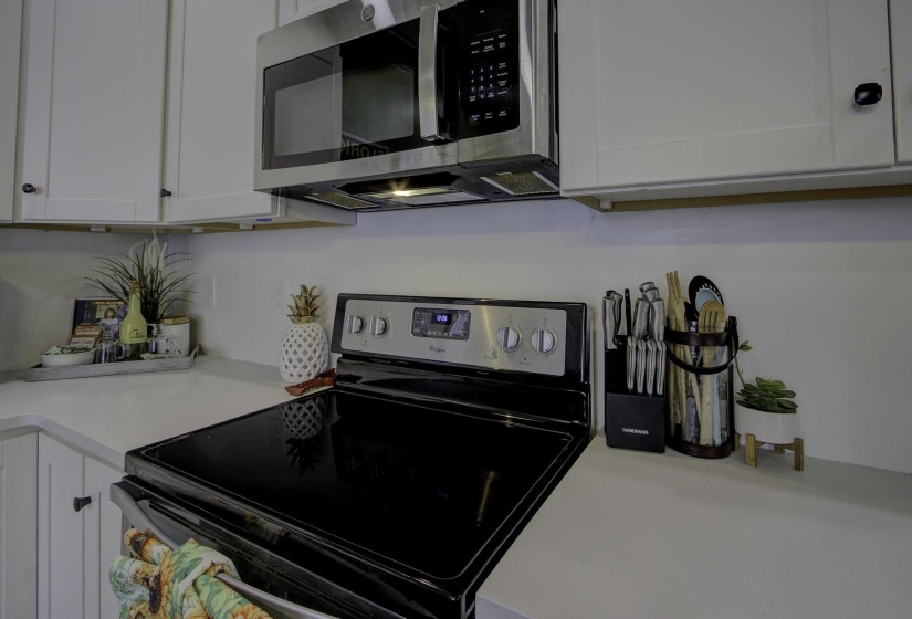 Kitchen with black / electric stove, white cabinets, and stainless steel microwave