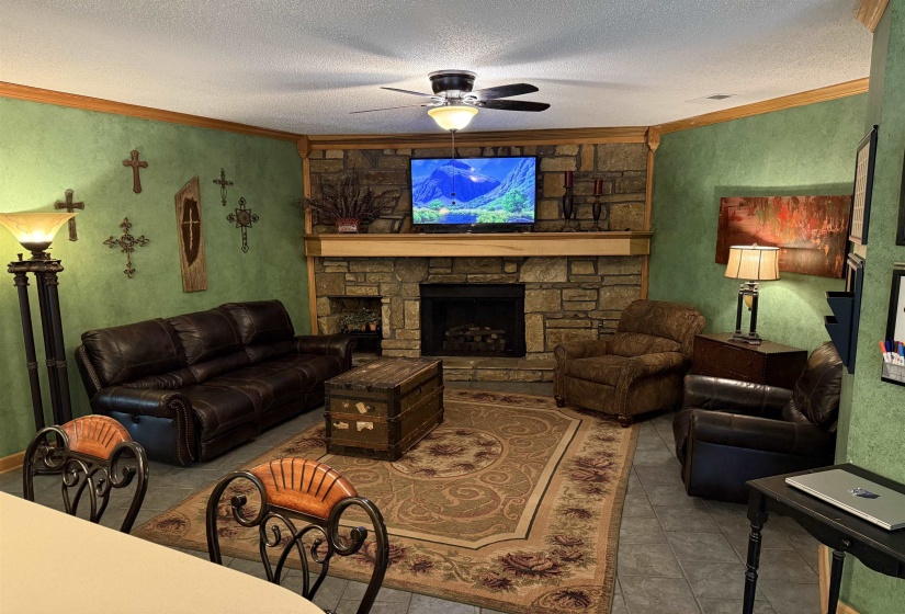 Tiled living room with ornamental molding, a textured ceiling, a textured wall, a stone fireplace, and ceiling fan